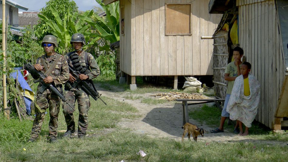 Photo by Girlie Linao. Lethal force: soldiers armed with machine guns stand alongside villagers in the southern Philippines.