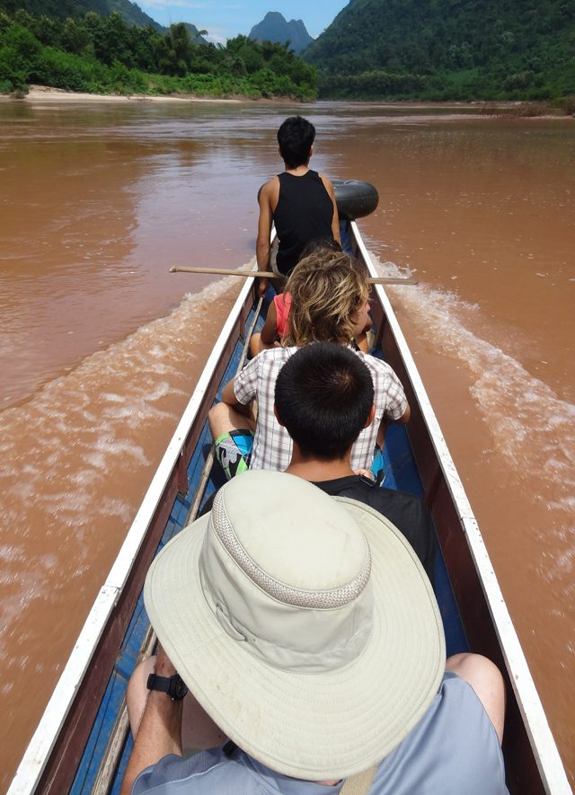 Photo by Matthew Crompton. Plain sailing: a longboat ferries visitors up the reddish waters of the Nam ou river for a spot of tubbing