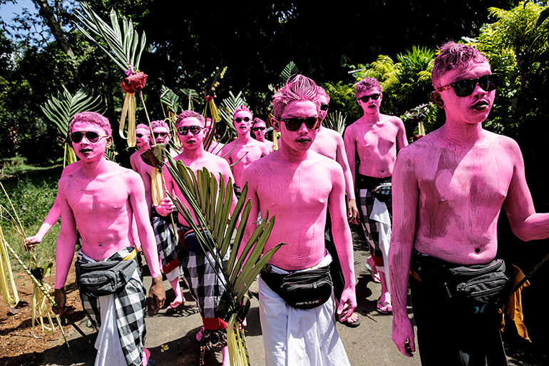 A group of boys covered in bright pink walk around Tegalalang village