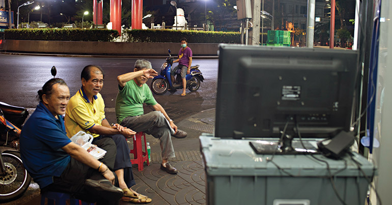 Men watch television on a street in Bangkok.