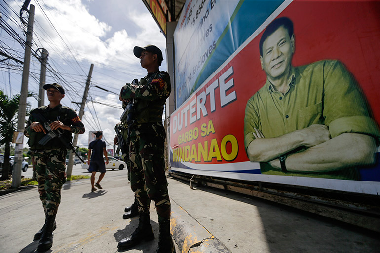 Filipino soldiers stand guard next to an election campaign poster displaying Philippine President Rodrigo Duterte (R), at a street in Davao City, southern Philippines,