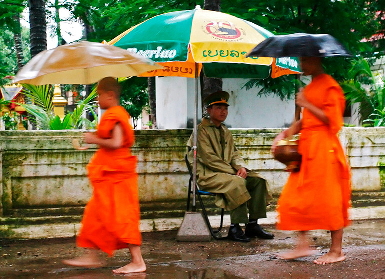 Laotian monks walking past a policeman at his guardpost in Vientiane, Laos