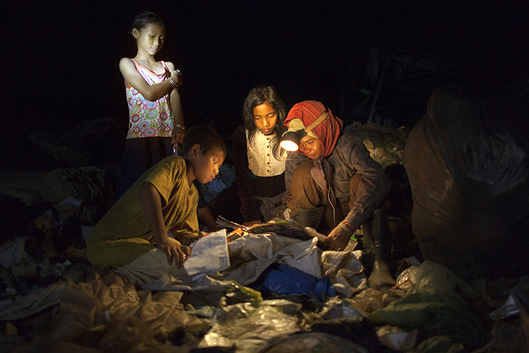 Child garbage pickers gather around to read a book they found as they work late at night recycling trash at a Siem Reap dump.