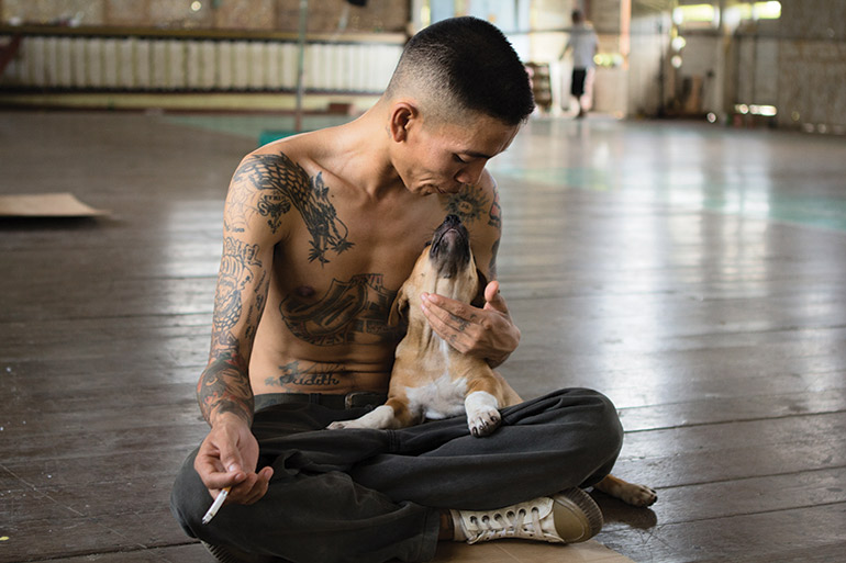 An inmate pets a dog while smoking a cigarette
