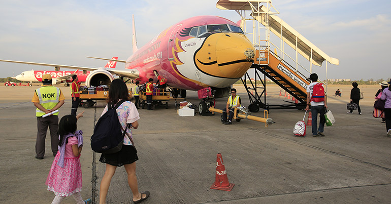 Airline passengers pass the nose of a Nok Air aircraft