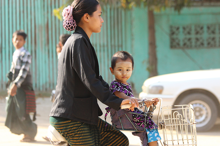 a woman cycles in Mandalay with her child in the front seat