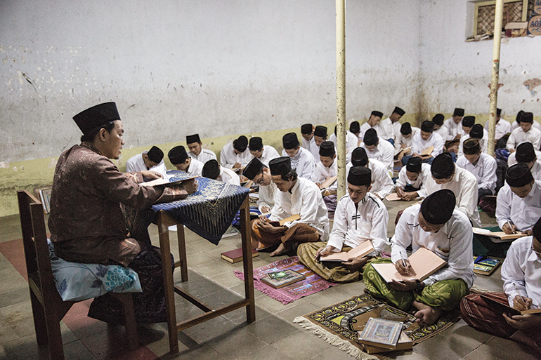 students sit on woven mats on the floor during a class