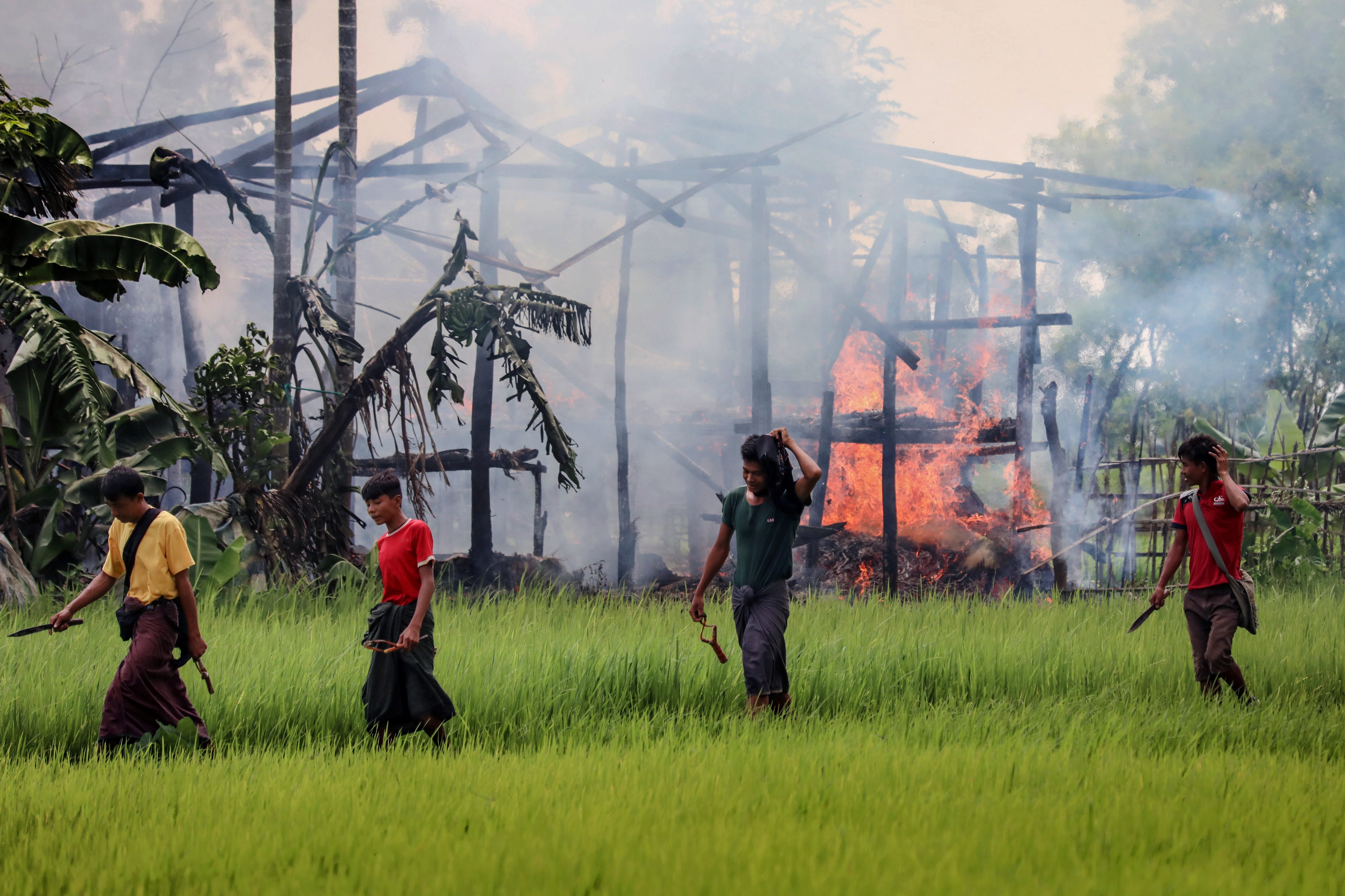 Unidentified men carry knives and slingshots as they walk past a burning house in Gawdu Tharya village near Maungdaw in Rakhine state in northern Myanmar in 2017. Photo: AFP