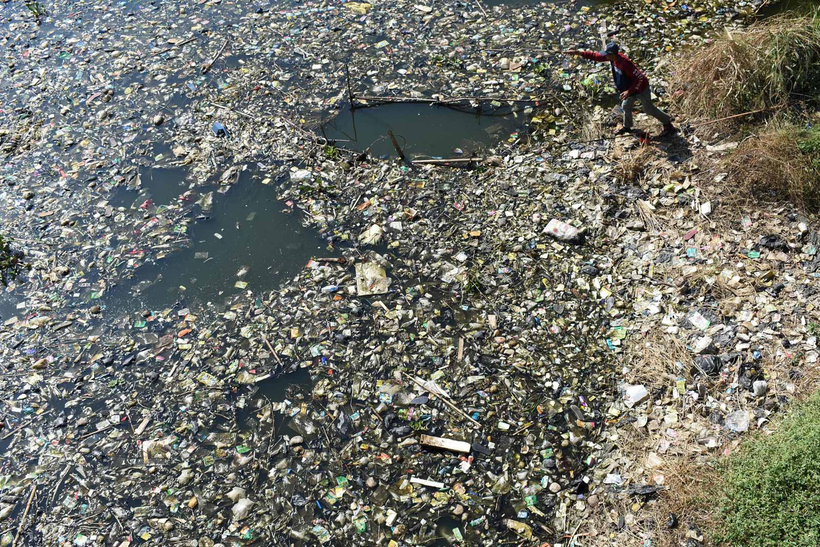 A scavenger collects plastic waste for recycling on the Citarum river choked with garbage and industrial waste, in Bandung, West Java province on June 26, 2019. - The river, one of the world's most polluted after decades of failed clean-up efforts, in 2018 was earmarked for revitalisation by Jakarta to make its water drinkable again by 2025.