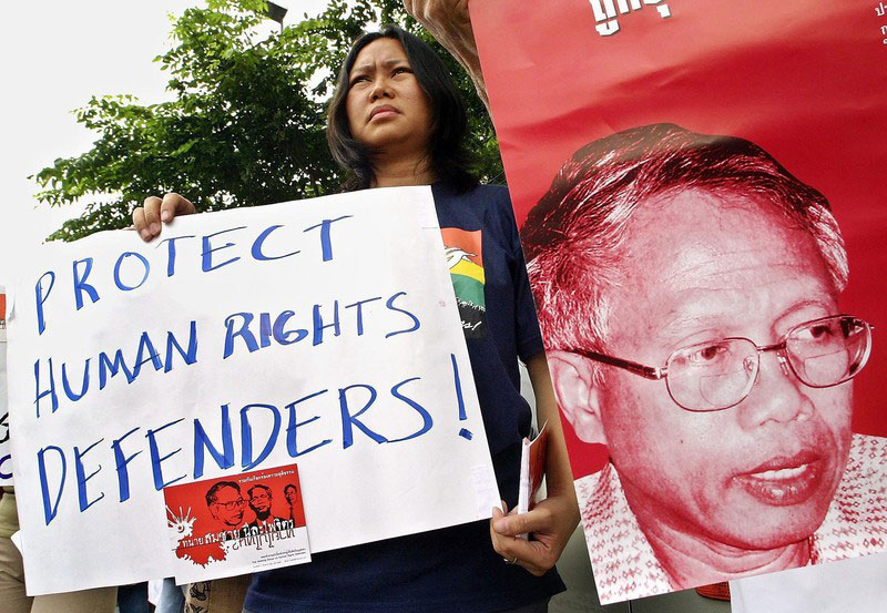 A Thai activist holds placard stands next to a photograph of missing lawyer Somchai Neelapaijit during a 2004 rally calling for an investigation into Somchai's disappearance earlier that year. Somchai's case remains unsolved. Photo: EPA