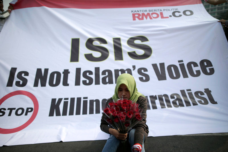 An Indonesian journalist holds flowers as she sits in front of a banner protesting the killing of journalists by ISIS in 2014. Photo: EPA/Mast Irham