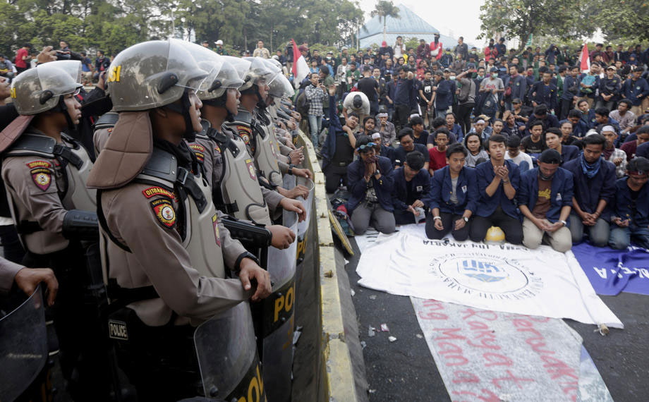 Indonesian students praying as riot policemen stand guard outside the parliament in Jakarta on 1 October 2019, during protests against new laws that proposed changing the criminal code and weakening the anti-corruption commission. Photo: EPA-EFE/Adi Weda